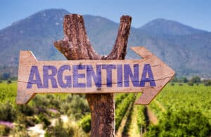 Wooden sign reading ARGENTINA points to the right over a vineyard with mountains in the background.